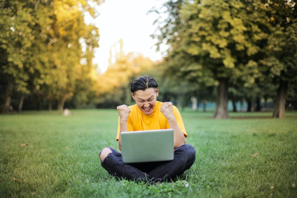 A happy man sitting on the grass in front of a laptop